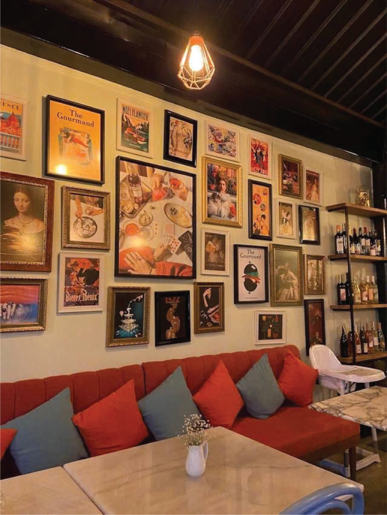 A cozy café interior with a red sofa, colorful throw pillows, and a gallery wall decorated with vintage-style posters.